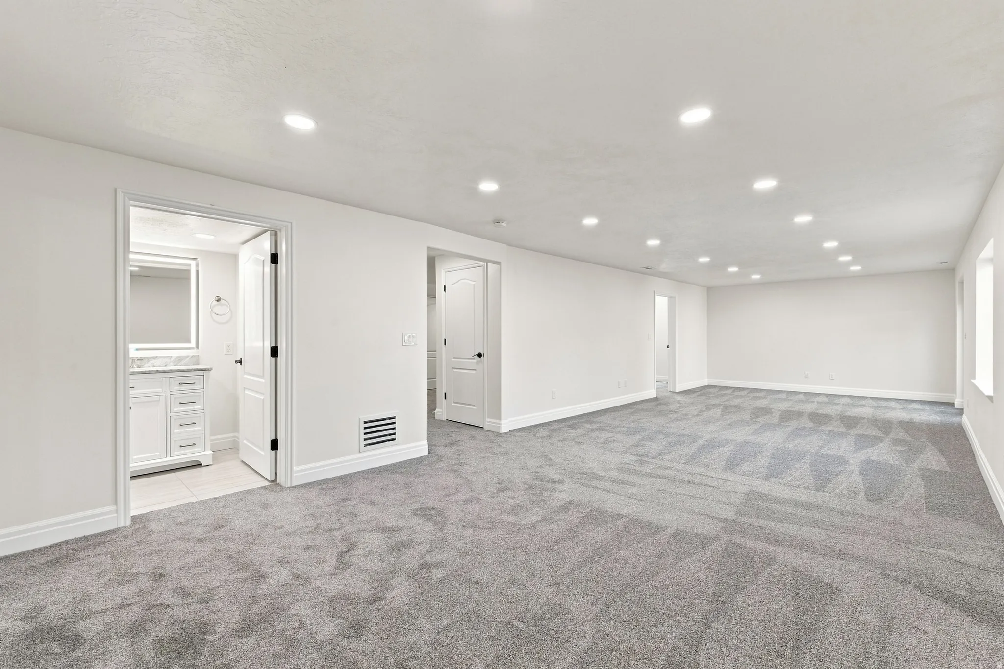 Expansive carpeted area with recessed lighting, white walls, and bright windows