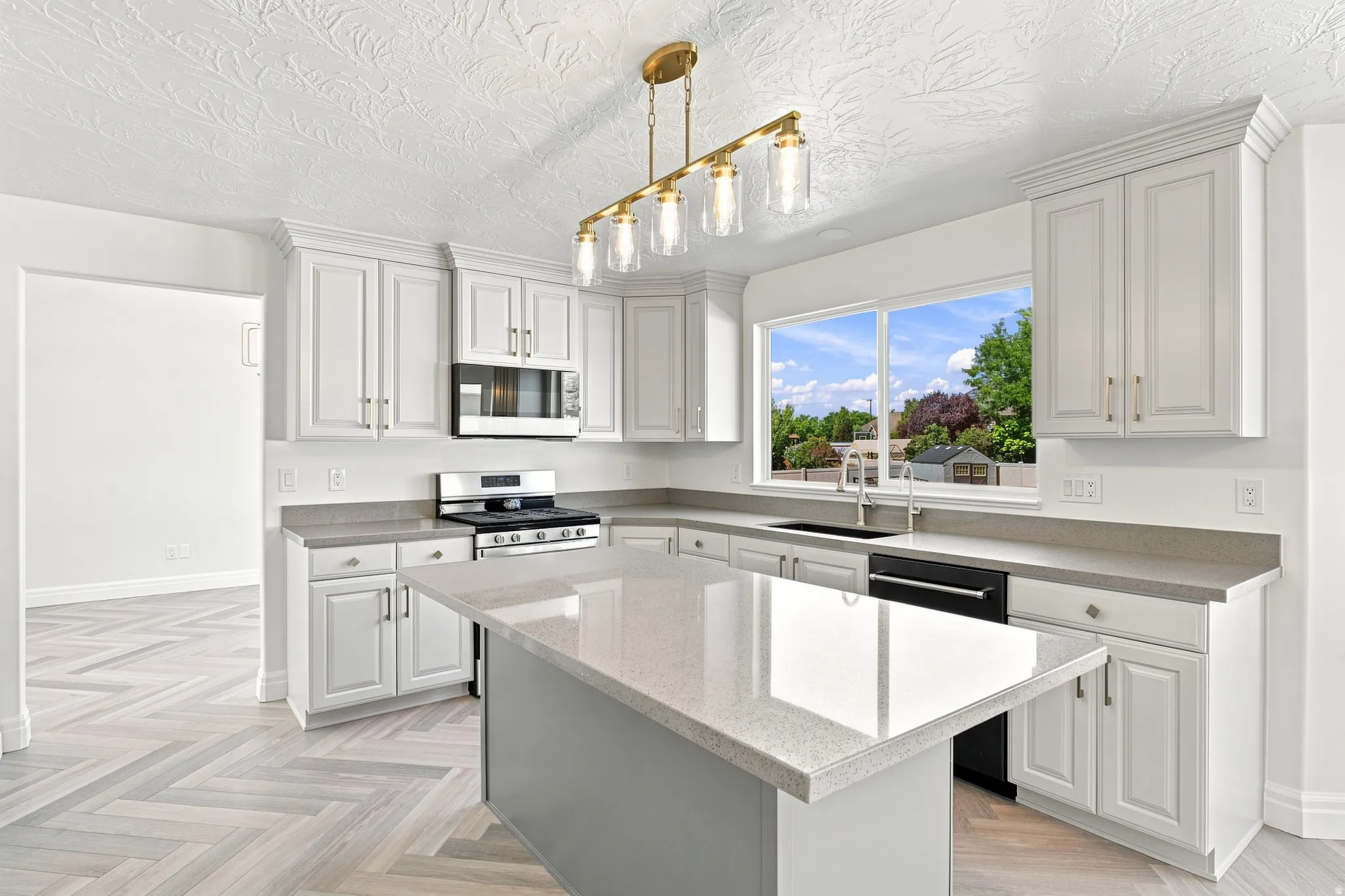 Kitchen featuring white cabinetry, light-toned countertops, a central island, a stainless steel gas range, and a brass-finish linear chandelier