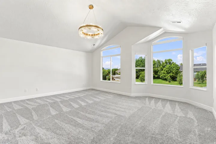 Vaulted ceiling with an ornate chandelier, multiple arched windows, patterned carpet, and white walls