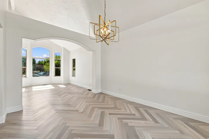 Herringbone wood-finish flooring, vaulted ceilings, arched entryways, and a contemporary chandelier