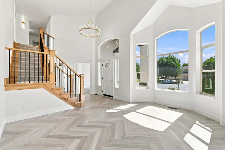 Vaulted entry with herringbone wood-finish flooring, a grand staircase featuring wood newels and wrought iron balusters, and a contemporary chandelier