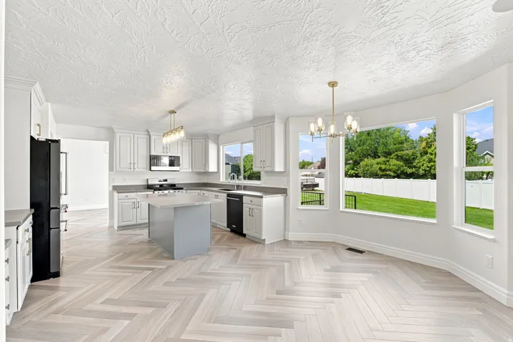 Contemporary kitchen featuring white cabinetry, a center island with a stone countertop, a full suite of black appliances, and light-toned wood-finish flooring in a herringbone pattern