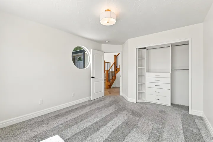 Built-in closet organization system, modern ceiling light fixture, accent round wall cut-out, white paneled interior door, and grey patterned carpet flooring