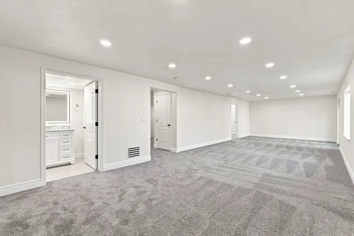Expansive carpeted area with recessed lighting, white walls, and bright windows