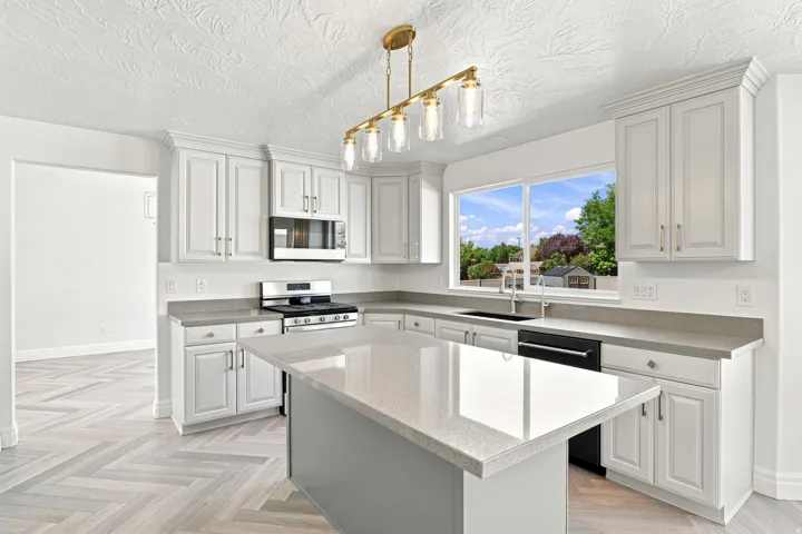 Kitchen featuring white cabinetry, light-toned countertops, a central island, a stainless steel gas range, and a brass-finish linear chandelier
