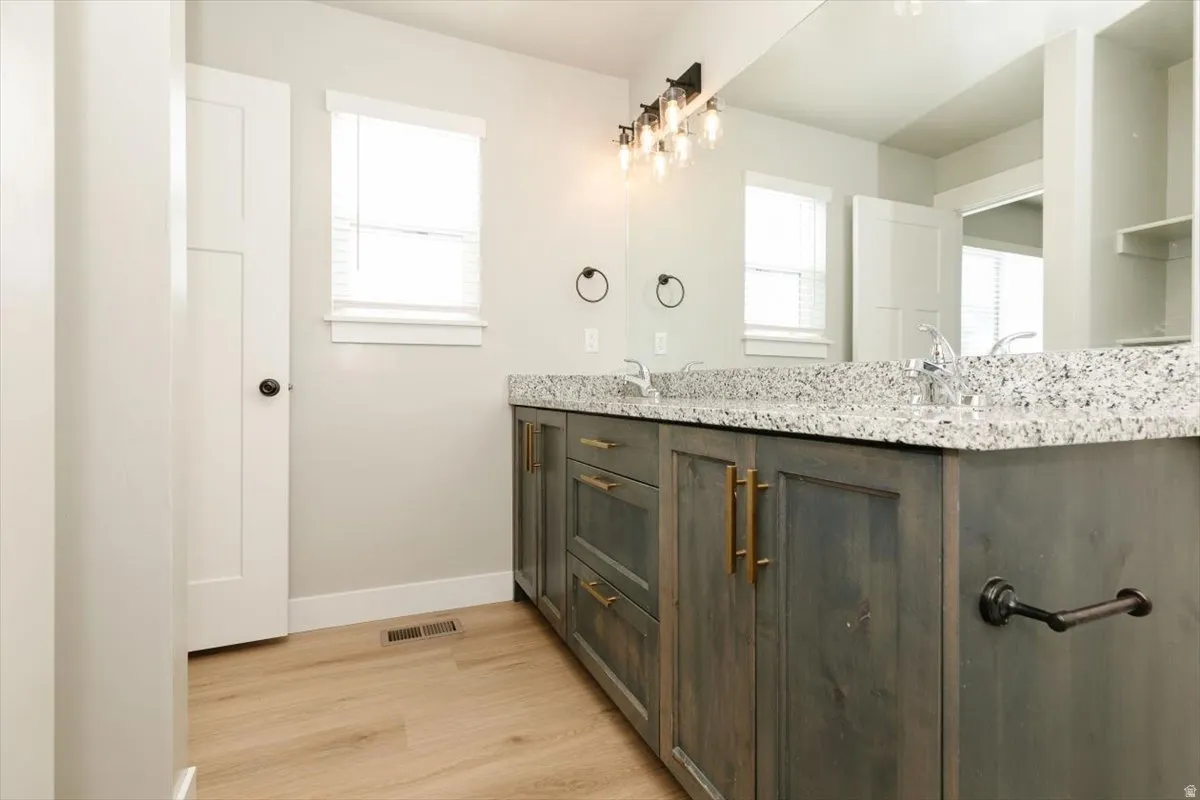 Dual sink vanity with a light-colored granite countertop, wood-finish cabinetry, and gold-tone hardware