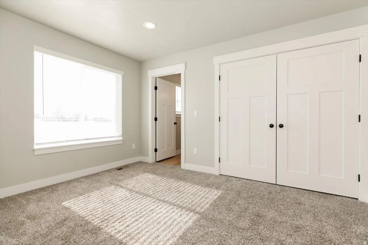 Carpeted room featuring a window with blinds, recessed lighting, and a closet with white paneled doors