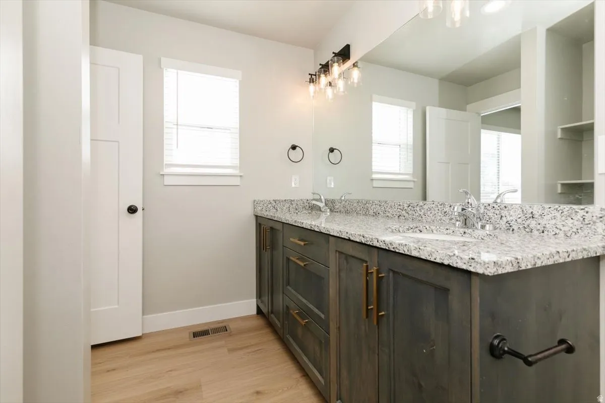 Dual sink vanity with stone-finish countertop, wood-finish cabinetry, and brushed nickel hardware