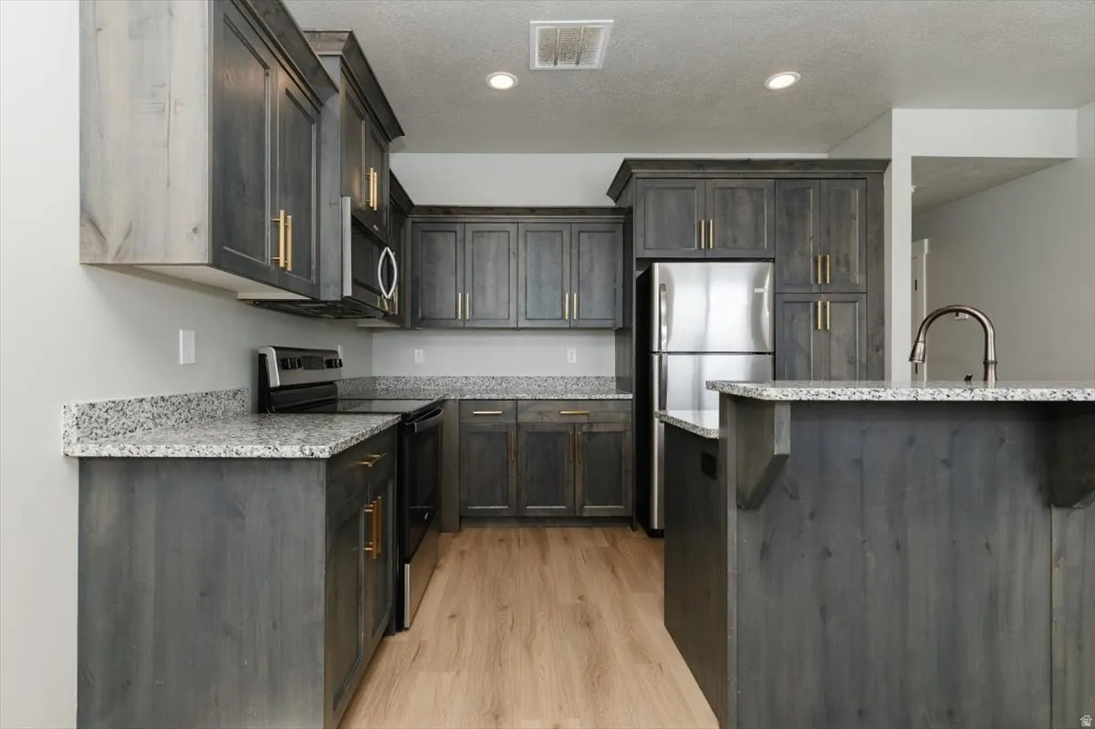 Expansive kitchen featuring wood-finish cabinetry, light-toned countertops, stainless steel appliances, and wood-finish flooring