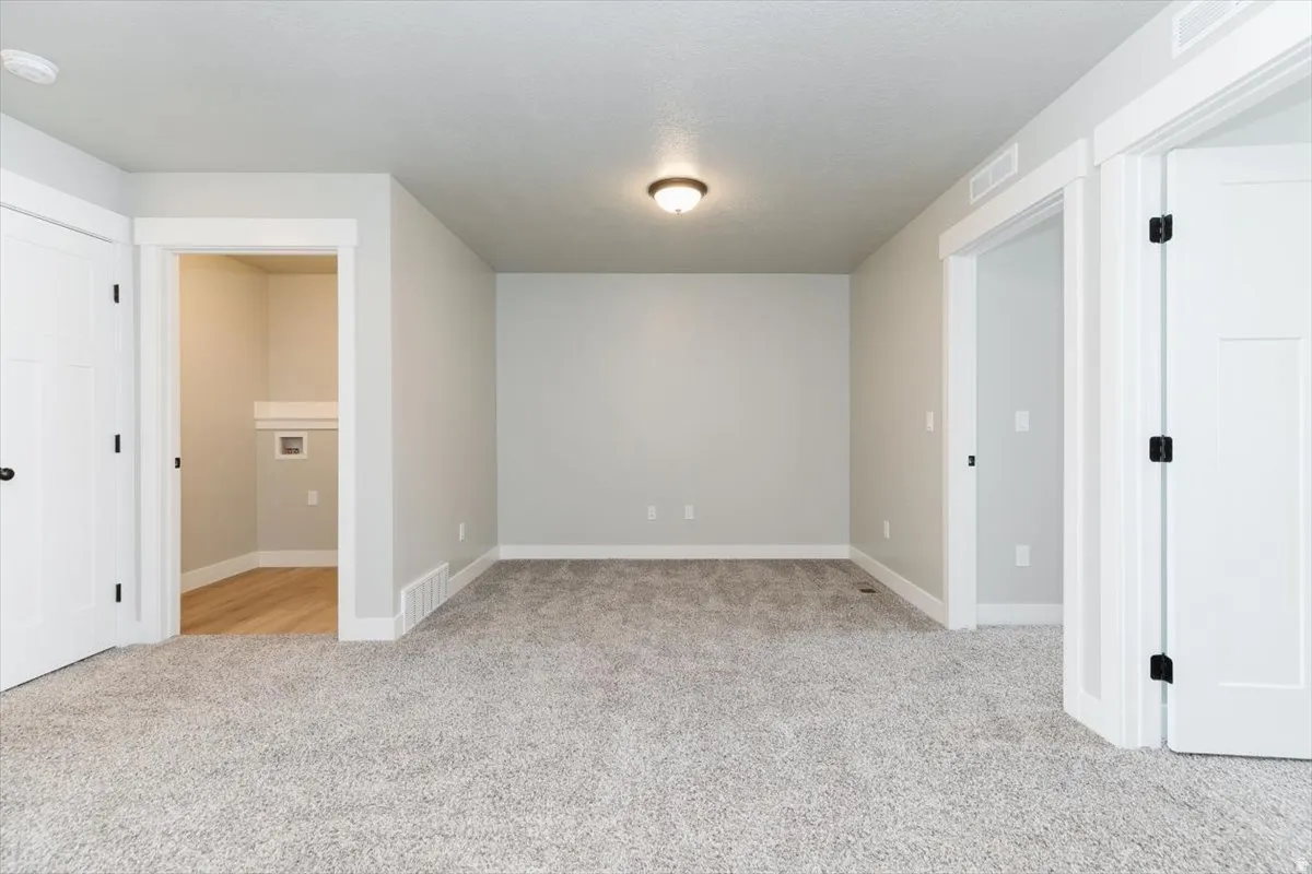 Light gray carpeting, white trim, recessed laundry area with wood-finish flooring, and white paneled doors