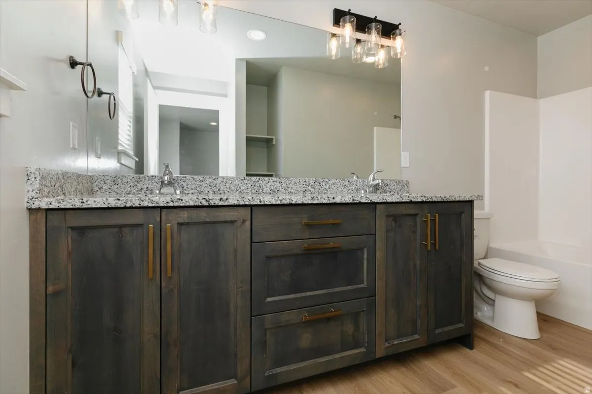 Dual sink vanity with stone countertop, wood-finish flooring, and a modern light fixture