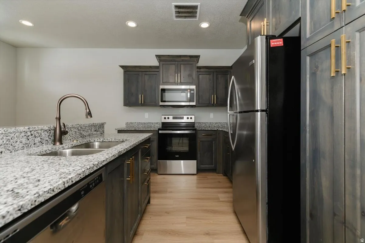 Kitchen featuring granite countertops, wood-finish flooring, stainless steel appliances, dark wood cabinetry, and recessed lighting