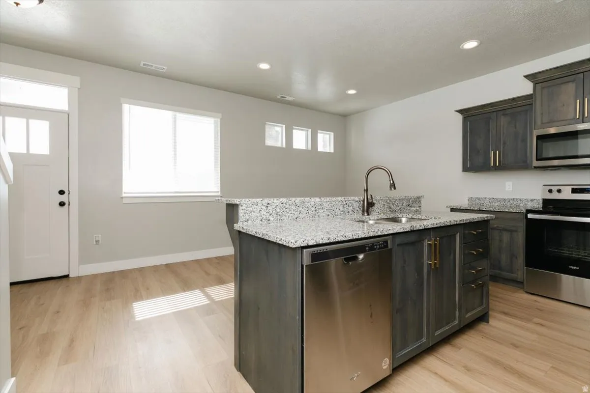 Kitchen featuring stainless steel appliances, speckled stone countertops, dark wood-finish cabinetry, and wood-finish flooring