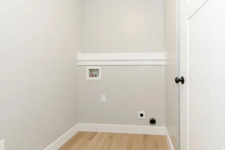 Laundry area featuring wood-finish flooring, crisp white trim, and a utility hookup