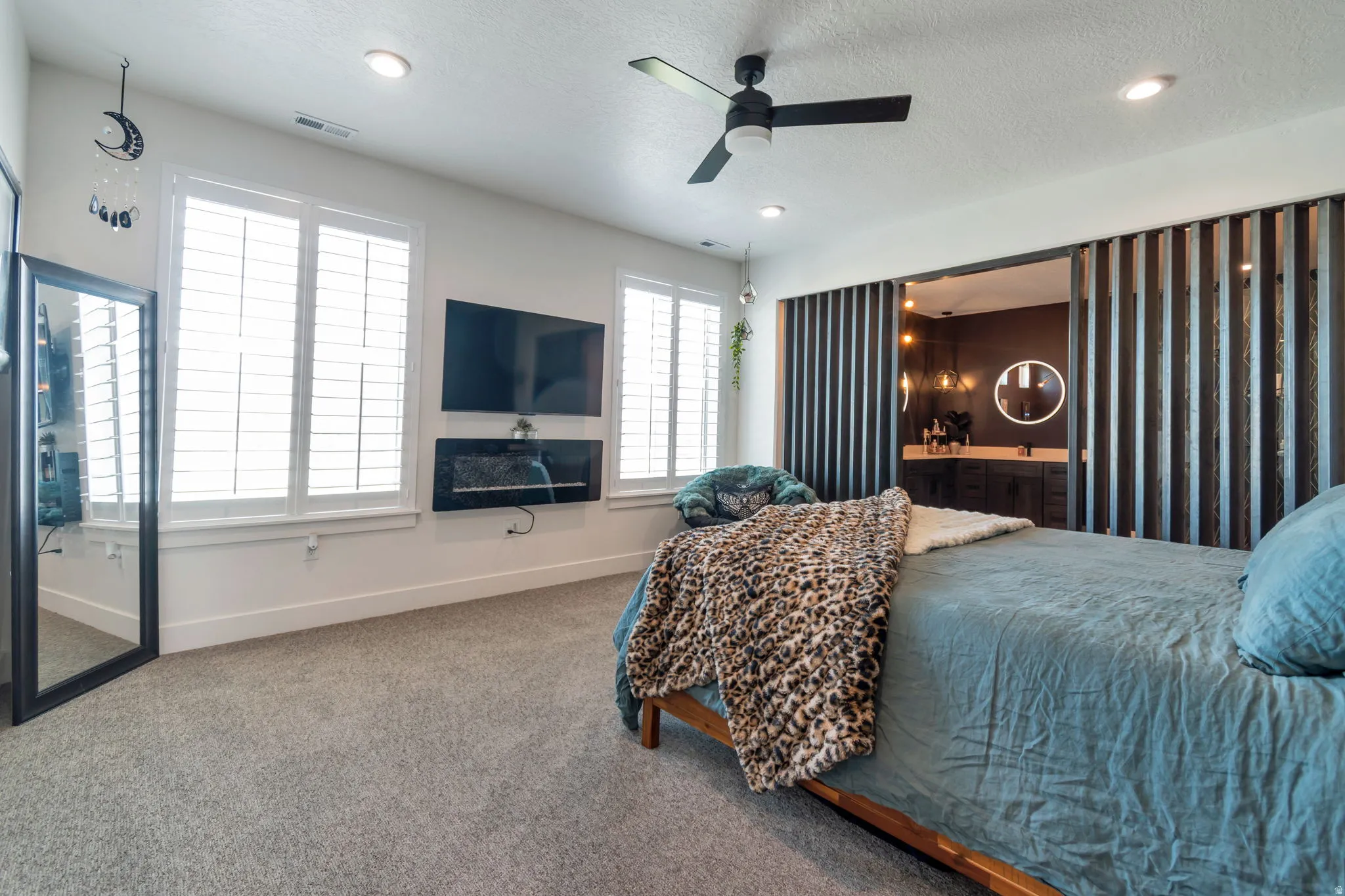 Recessed lighting, ceiling fan, twin windows with plantation shutters, wall-mounted electric fireplace, and dark-toned sliding slat doors