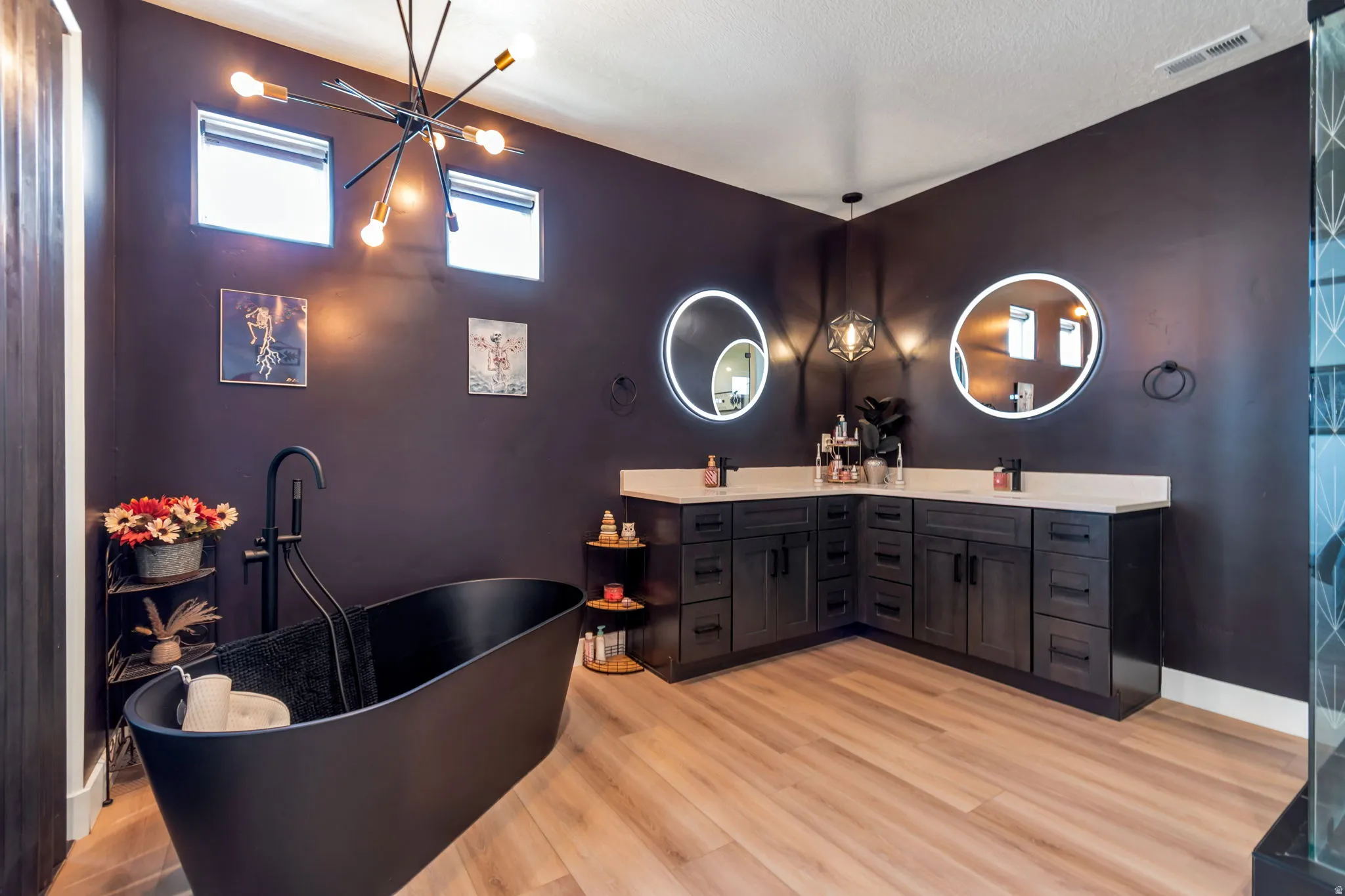 Freestanding soaking tub with floor-mounted faucet, dual vanity with solid surface countertops, and wood-finish flooring