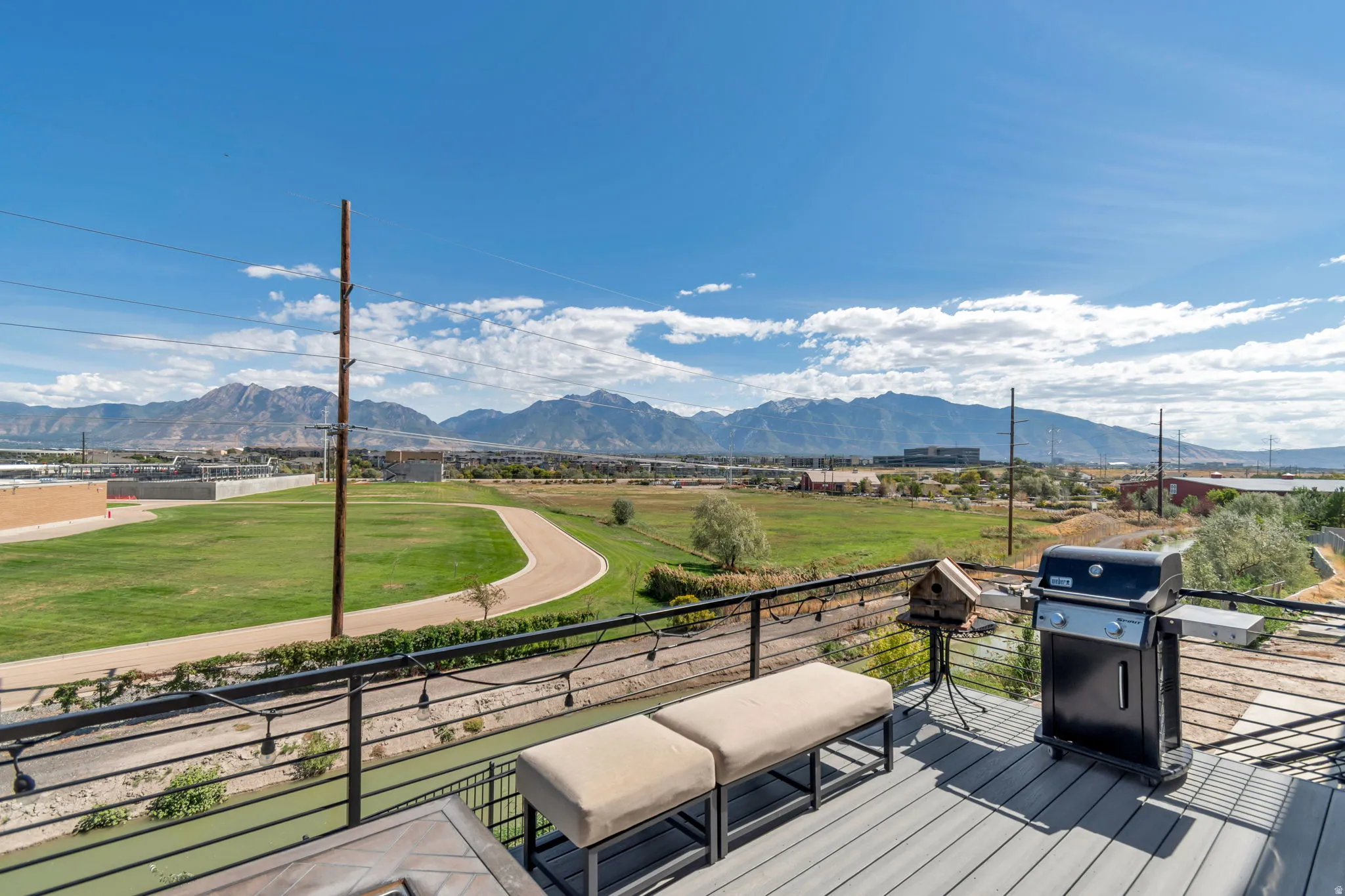 Expansive mountain scenery framing a green landscape, visible from a private deck featuring composite decking, a metal railing, and string lighting