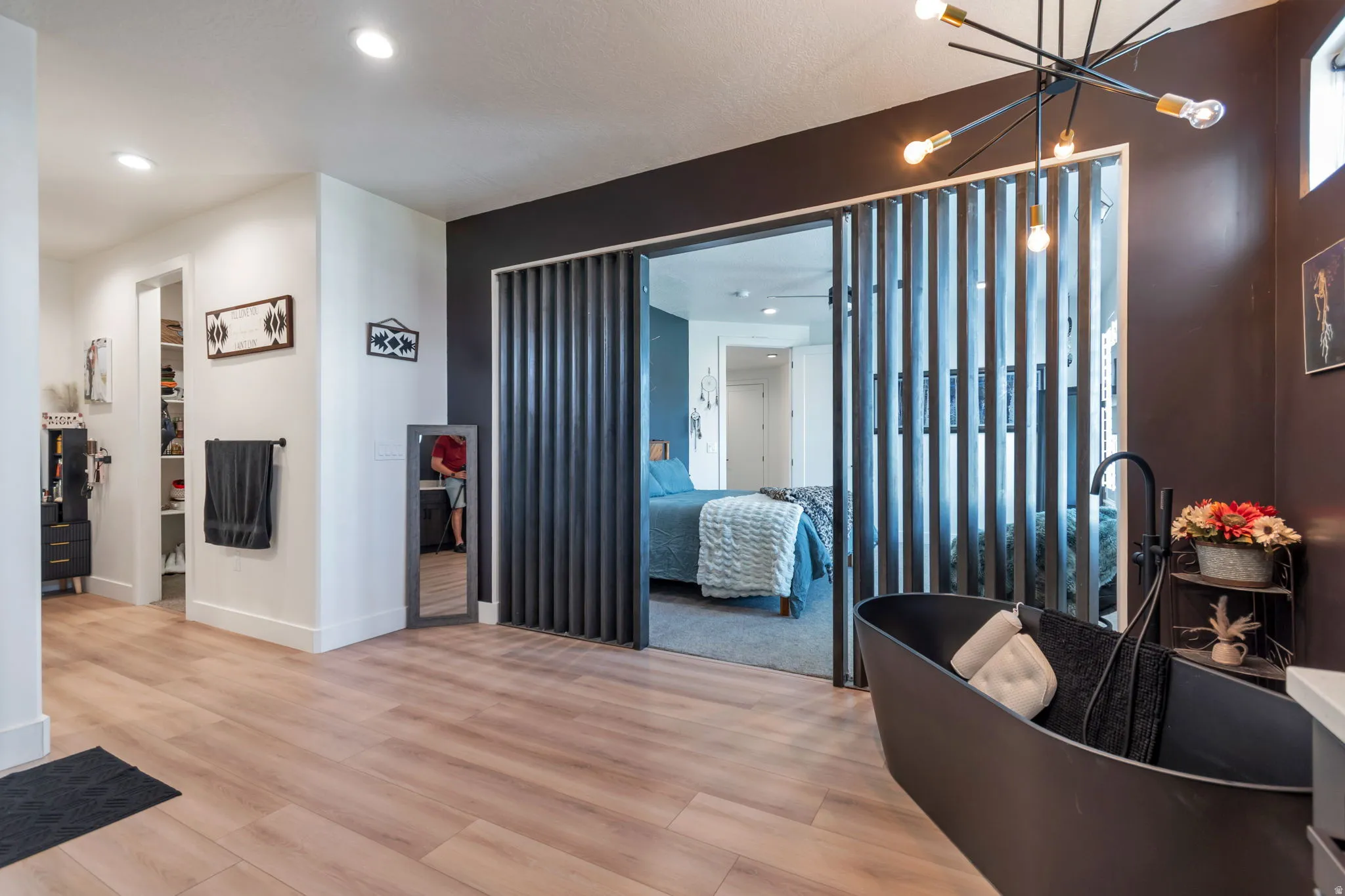 Wood-finish flooring, recessed lighting, slat-style sliding doors, freestanding soaking tub with matte black fixtures, and a modern sputnik chandelier