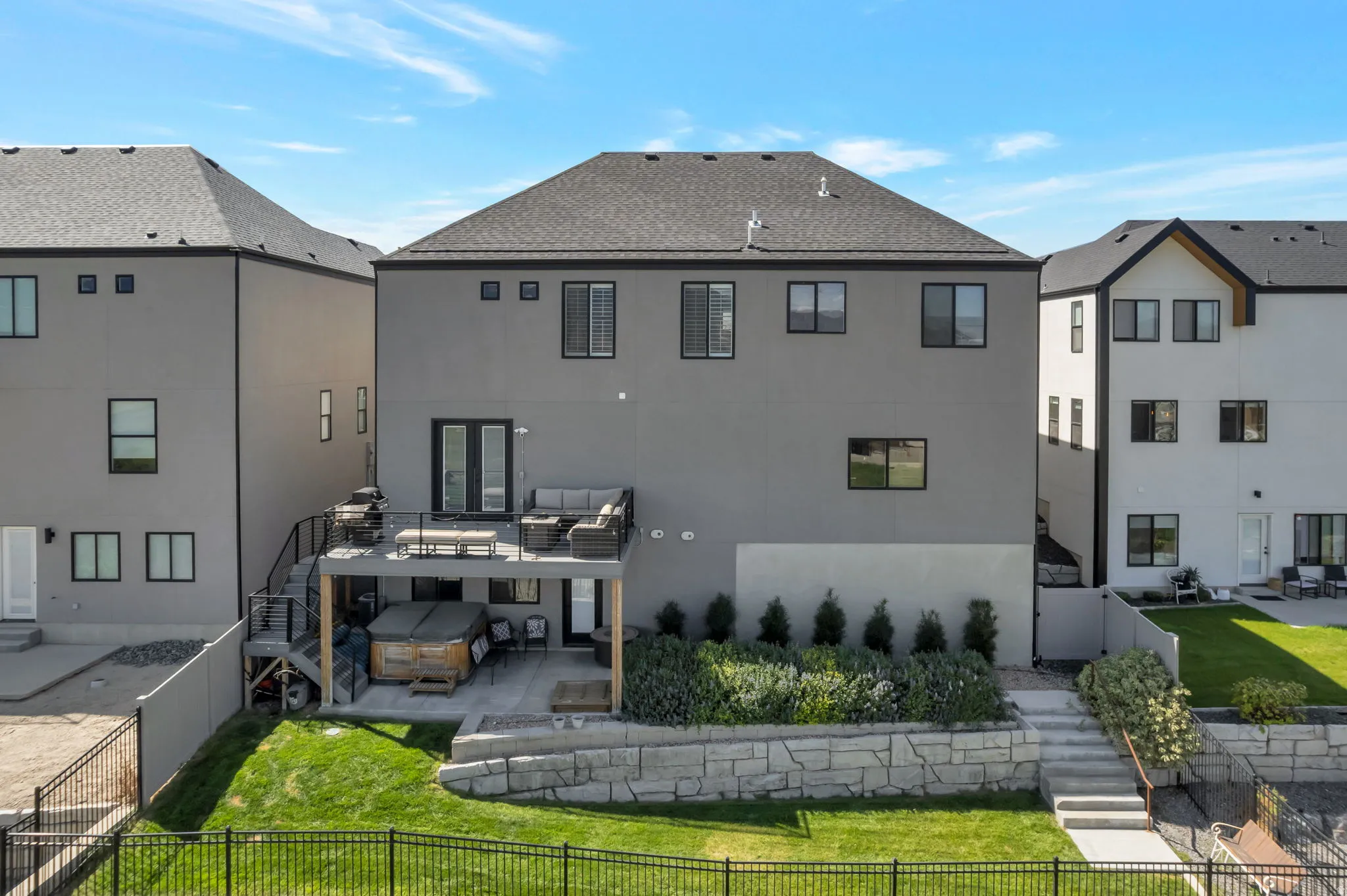 Multi-level backyard featuring a deck with dark railings, a ground-level patio, a tiered retaining wall, and a landscaped garden bed