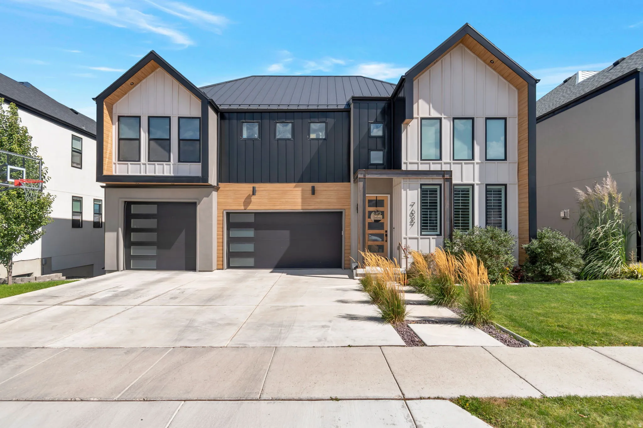 Modern exterior featuring vertical siding, metal roofing, wood-look accents, a two-car garage with frosted glass panels, and a concrete driveway