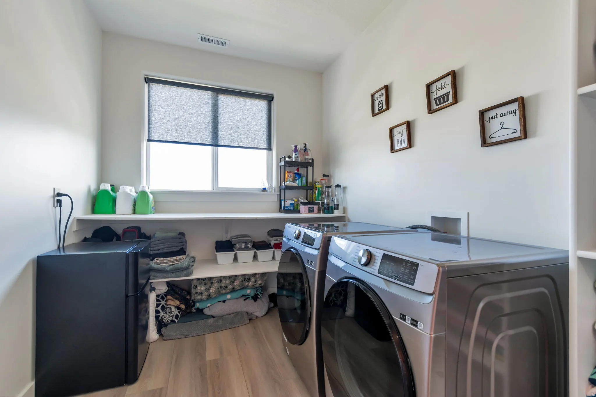 Integrated laundry area with wood-finish flooring, a window with roller shade, and built-in shelving