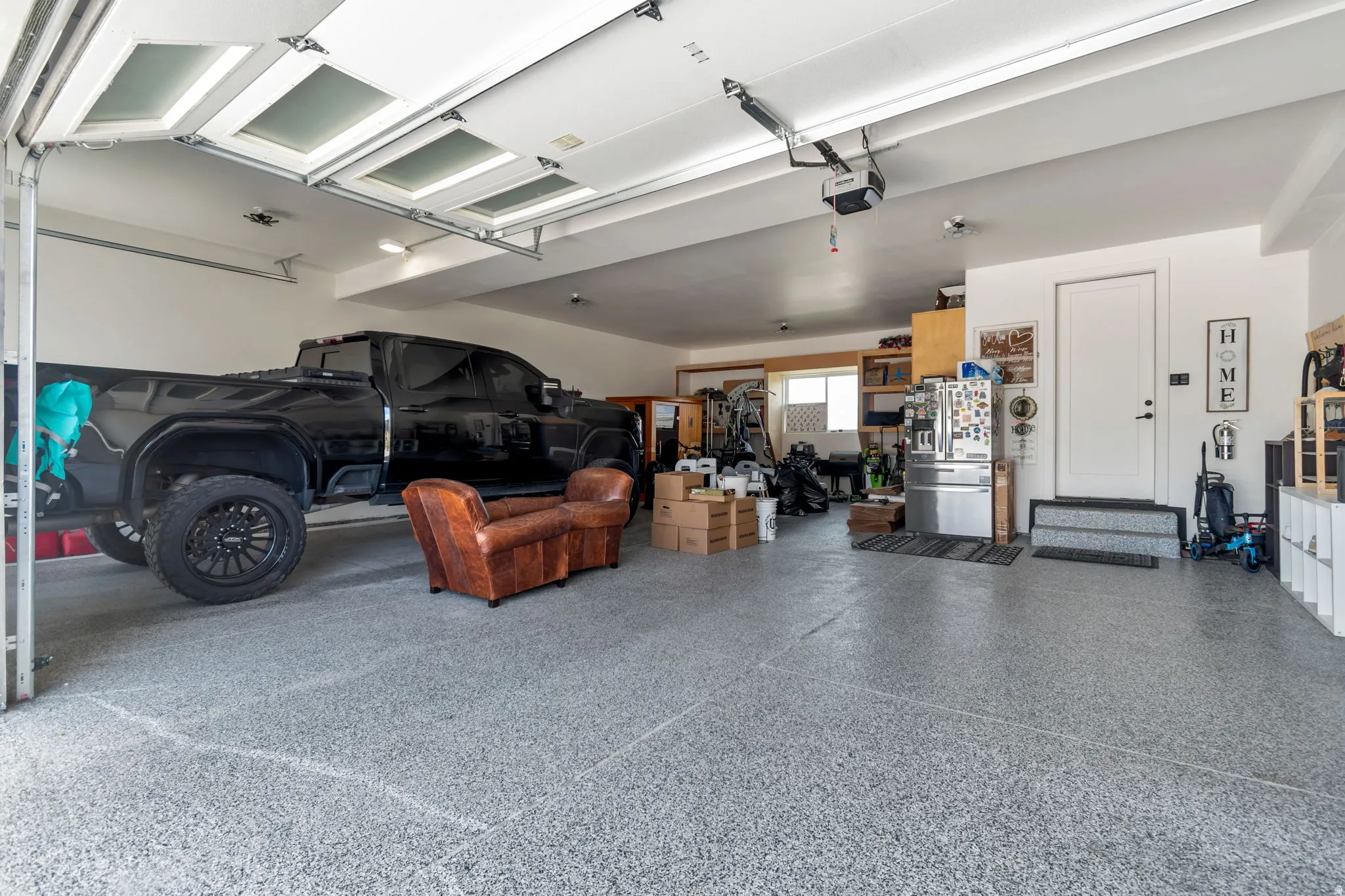 Spacious garage featuring a durable epoxy floor, overhead lighting, an automatic garage door opener, and a panel-style access door