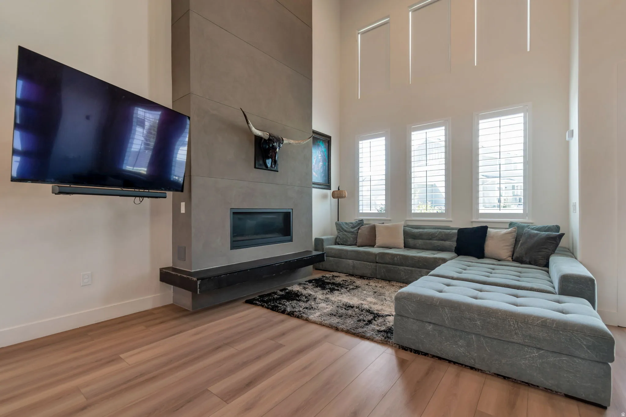 High ceilings, wood-finish flooring, concrete-finish fireplace surround, built-in linear fireplace, and three windows with white plantation shutters