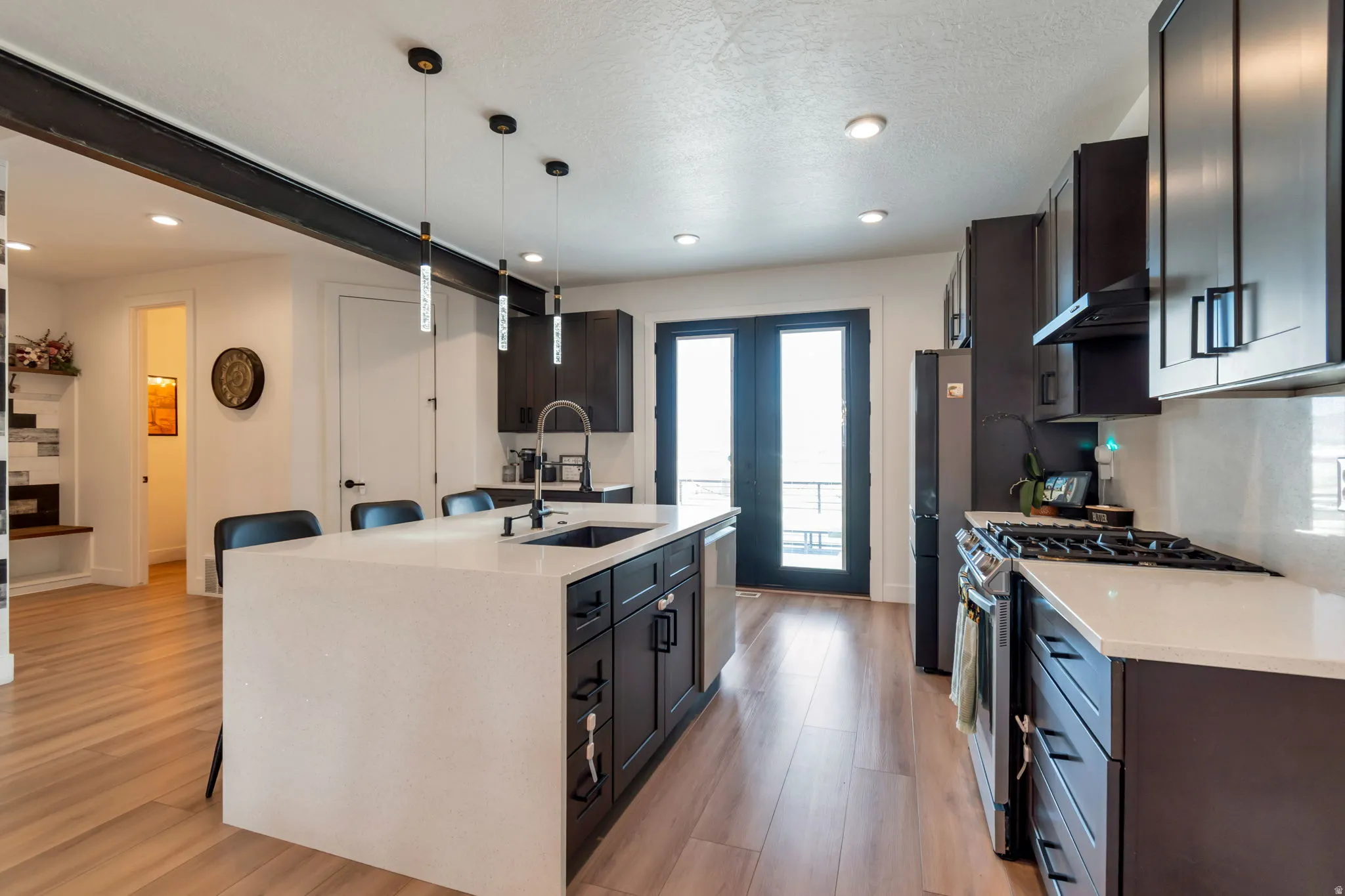 Kitchen featuring an island with built-in sink, dark cabinetry, light countertops, wood-finish flooring, and recessed lighting