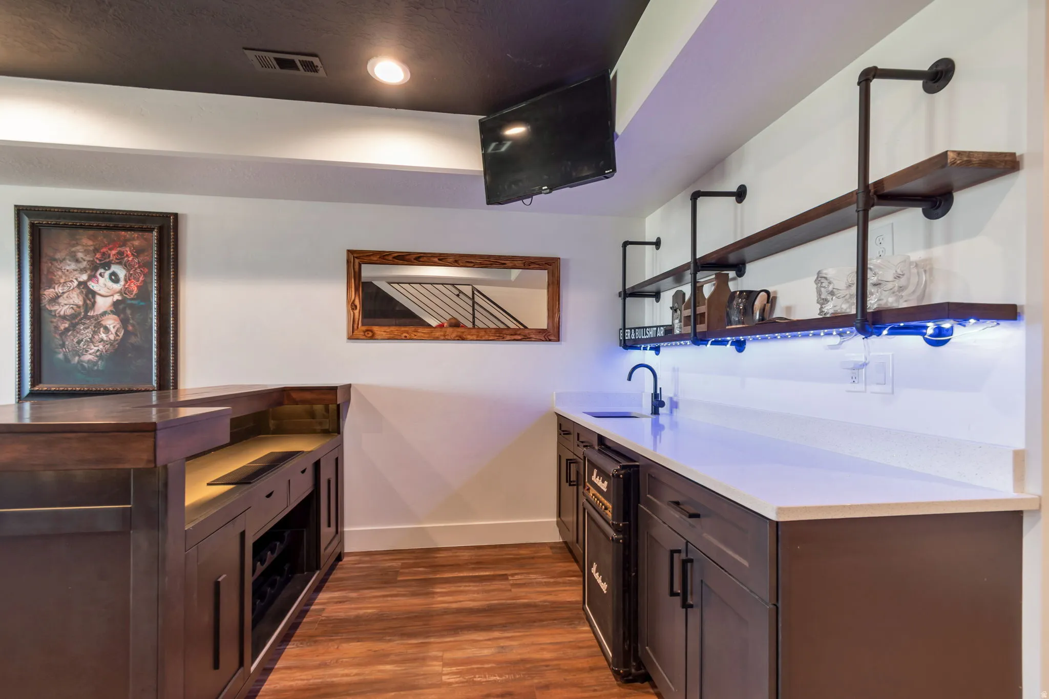 Built-in wet bar with wood-finish flooring, dark cabinetry, recessed lighting, and open shelving