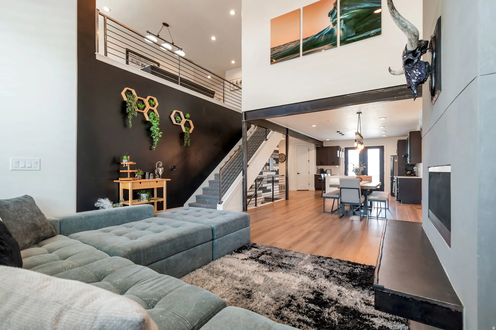 Two-story living area with high ceilings, wood-finish flooring, a modern fireplace, and an open-concept layout extending to the kitchen and dining areas