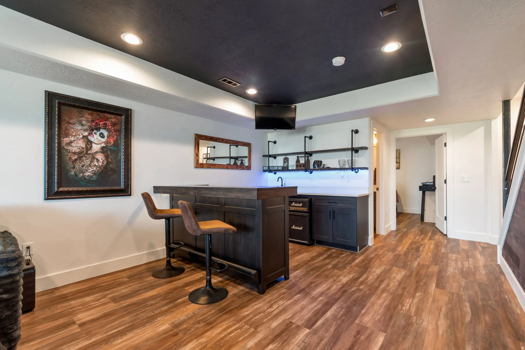 Wood-finish flooring, recessed lighting, built-in bar, built-in shelving, and dark ceiling treatment