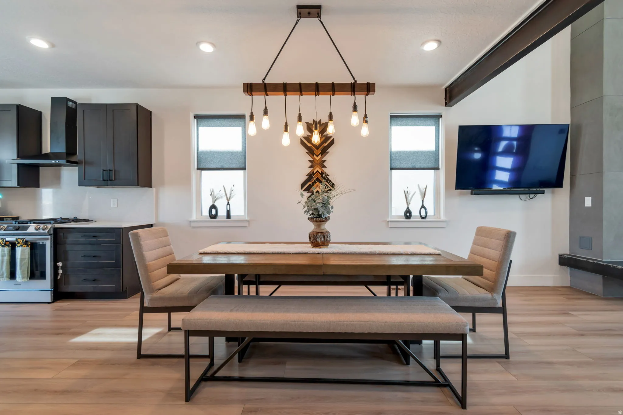 Open-concept dining area featuring wood-finish flooring, a contemporary chandelier, recessed lighting, dark cabinetry, and a modern range hood