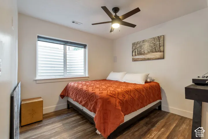 Room featuring wood-finish flooring, a ceiling fan with integrated lighting, and a window with blinds