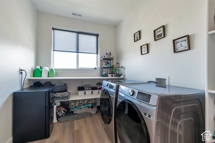 Integrated laundry area with wood-finish flooring, a window with roller shade, and built-in shelving