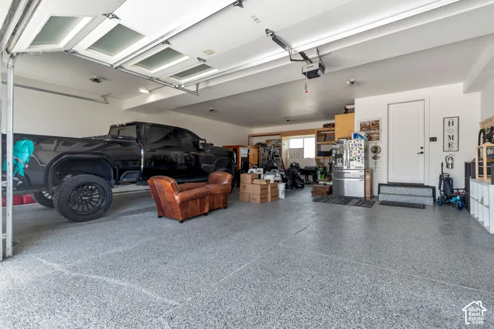 Spacious garage featuring a durable epoxy floor, overhead lighting, an automatic garage door opener, and a panel-style access door