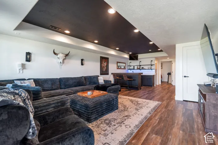 Wood-finish flooring throughout, featuring a built-in wet bar with shelving, a recessed ceiling with integrated lighting, and a solid core interior door