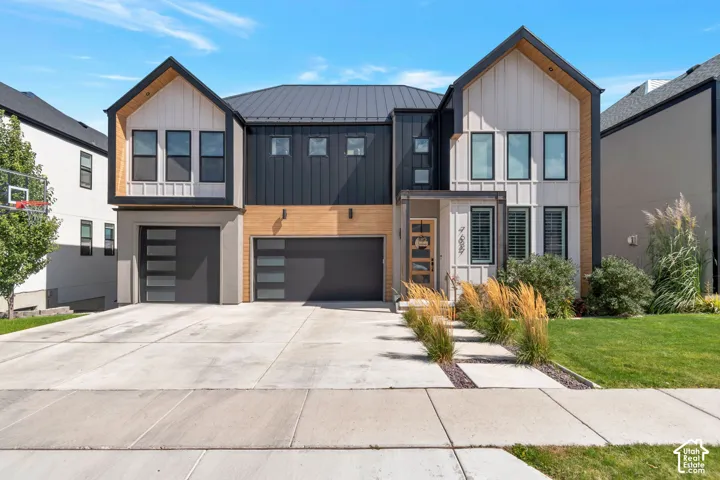 Modern exterior featuring vertical siding, metal roofing, wood-look accents, a two-car garage with frosted glass panels, and a concrete driveway