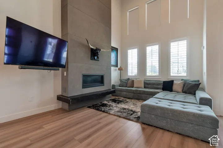 High ceilings, wood-finish flooring, concrete-finish fireplace surround, built-in linear fireplace, and three windows with white plantation shutters