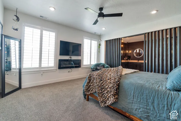 Recessed lighting, ceiling fan, twin windows with plantation shutters, wall-mounted electric fireplace, and dark-toned sliding slat doors