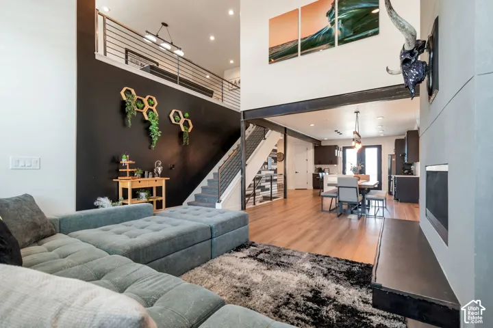 Two-story living area with high ceilings, wood-finish flooring, a modern fireplace, and an open-concept layout extending to the kitchen and dining areas