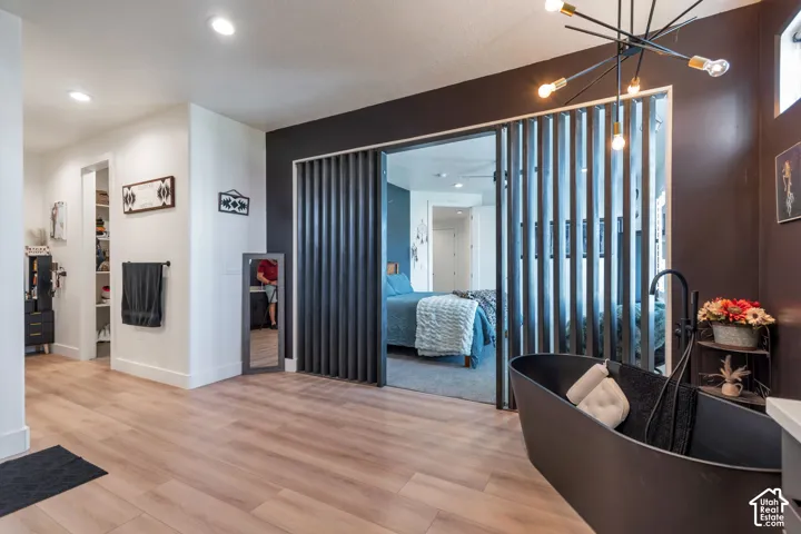 Wood-finish flooring, recessed lighting, slat-style sliding doors, freestanding soaking tub with matte black fixtures, and a modern sputnik chandelier