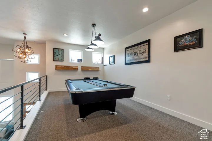 Loft space featuring carpeted flooring, a black metal railing, recessed lighting, and multiple windows