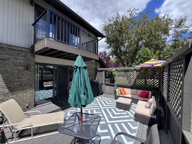 Outdoor deck with wood-finish flooring, lattice privacy screens, and an upper-level balcony featuring dark railings