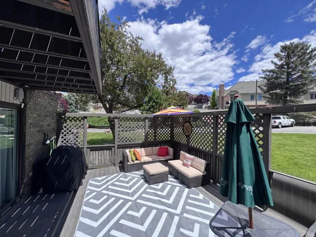 Spacious outdoor deck featuring privacy lattice, a brick-finish wall, and a slatted overhead cover