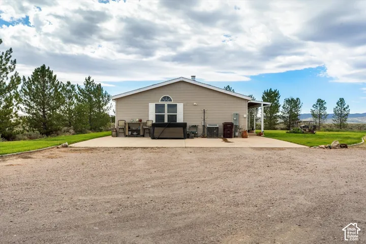 Spacious gravel parking area, expansive concrete patio, mature evergreen trees, and a covered porch with white columns