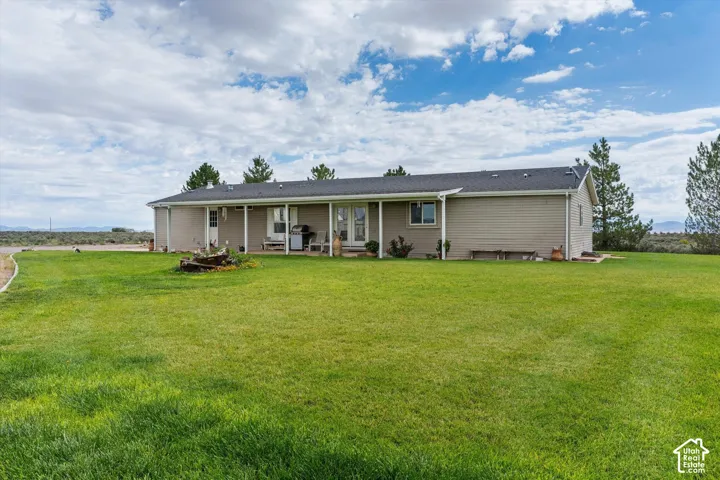 Expansive lawn with a covered back patio, tan siding, and a dark roof