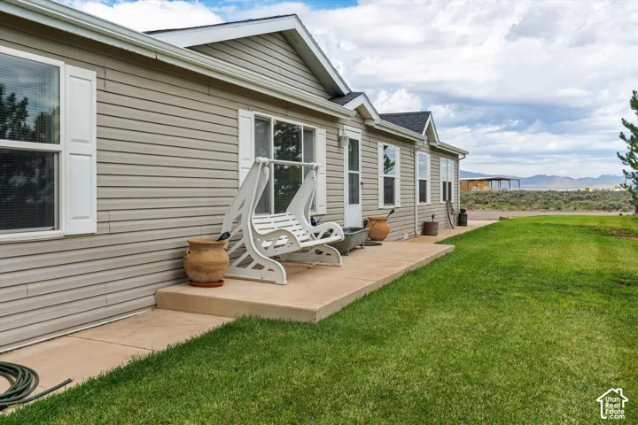 Siding exterior with multiple windows, a concrete patio, and a grass lawn