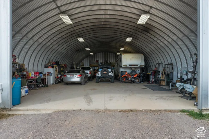 Quonset hut structure featuring an arched corrugated metal roof, concrete flooring, and overhead fluorescent lighting
