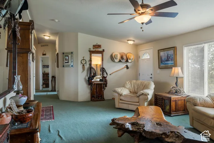 Expansive living area featuring a ceiling fan with integrated lighting, a front entry door with decorative glass, and a large window with blinds