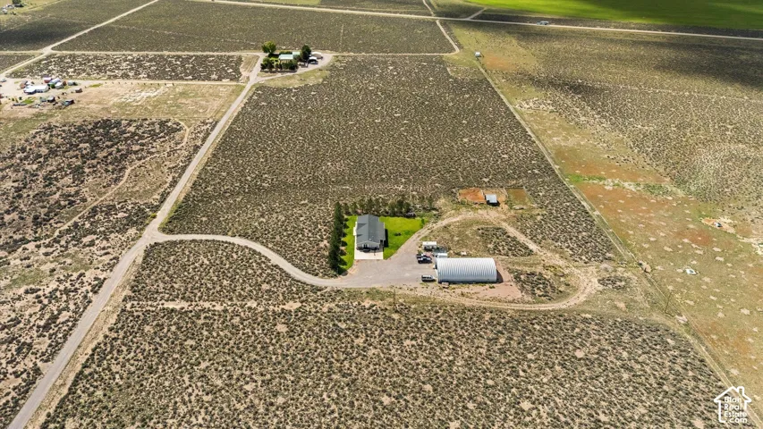 Single-story residence on expansive land featuring a metal outbuilding, gravel drive, and a defined green lawn area